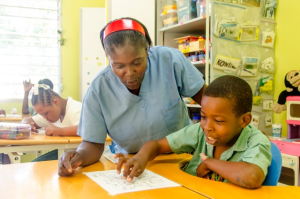 Teacher Delicarme Chery assists 12 year old Fabenson during art class. Photo: NPH Haiti.